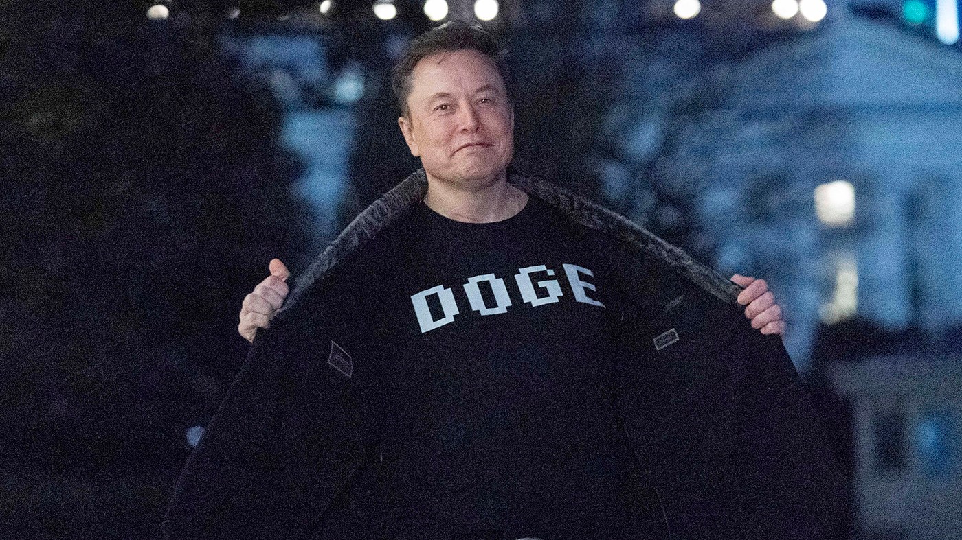 Elon Musk flashes his T-shirt that reads “DOGE” to the media as he walks on South Lawn of the White House, in Washington, March 9, 2025.