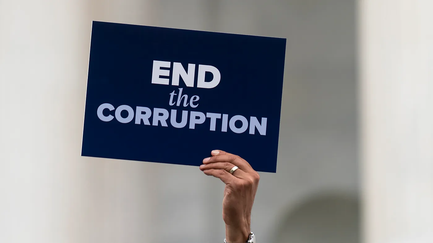 Sen. Alex Padilla (D-Calif.) holds a sign reading “End the Corruption” during a press event with House and Senate Democrats to discuss the Republicans’ budget proposals outside the Senate Chamber on May 21, 2026.