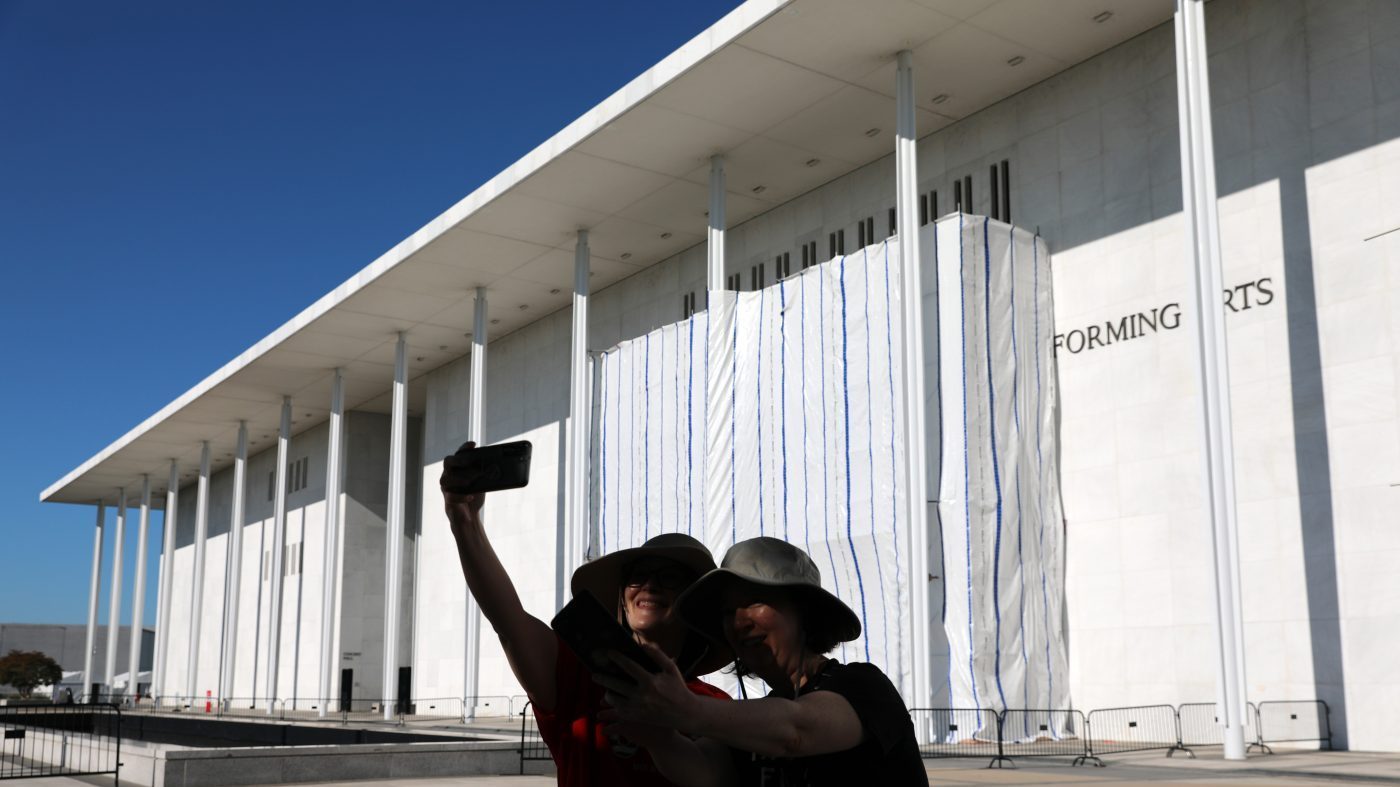 Women take a selfie as the wall of the John F. Kennedy Center for the Performing Arts is covered in tarp as work continues on the removal of President Donald Trump’s name, Saturday, June 13, 2026 in Washington. (AP Photo/Rahmat Gul)