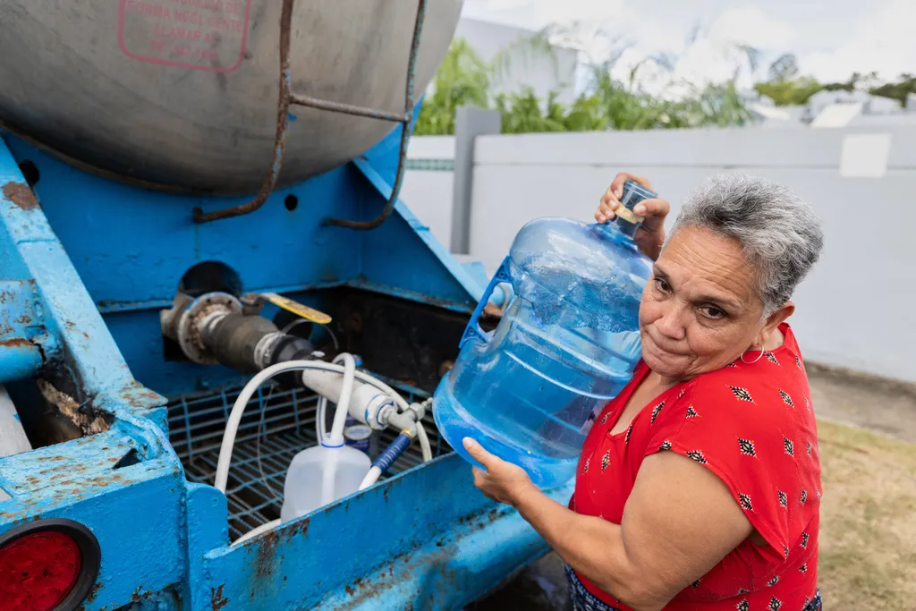 A woman lifts a jug she filled with water from a tanker truck amid rationing caused by drought, in the Cupey sector of San Juan, Puerto Rico, Wednesday, Aug. 5, 2026. (AP Photo/Alejandro Granadillo)