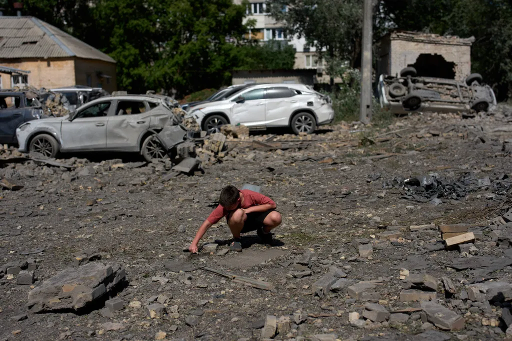 A youth removes scattered debris next to cars destroyed by an overnight Russian missile and drone attack on Kyiv, Ukraine, Thursday, Aug. 20, 2026 (AP Photo/Francisco Seco)