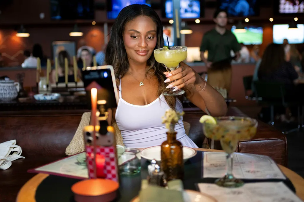Phoenix-based content creator holds up a house margarita while filming content during the grand opening of Padeland, a venue for the racket sport padel in Chandler, Ariz., Thursday, Aug. 13, 2026. (AP Photo/Rebecca Noble)