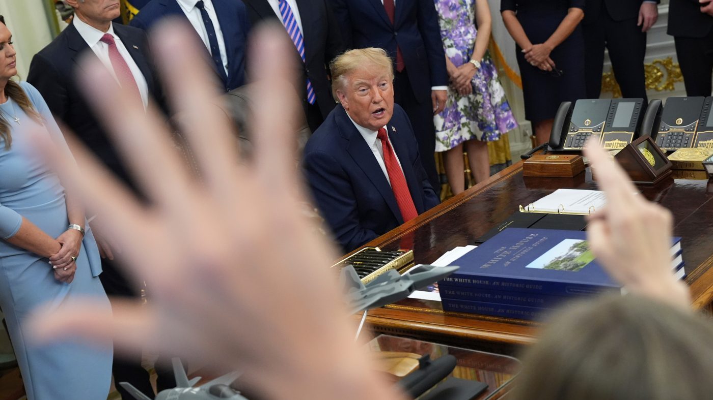 Reporters raise hands to ask a question as President Donald Trump, seated, speaks during an event about healthcare in the Oval Office of the White House, Friday Sept. 18, 2026, in Washington. (AP Photo/Jacquelyn Martin)