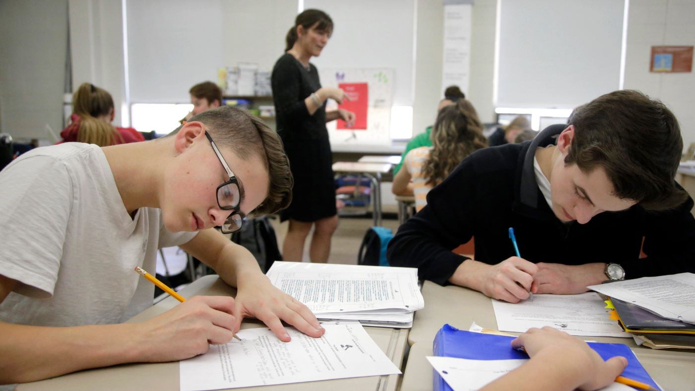 In this Wednesday, March 8, 2017 photo, high school students Jackson Laferriere, left, and Noah Lemoine fill out work sheets as teacher Natalie O’Brien, top center, speaks with students during a civics class called “We the People,” at North Smithfield High School in North Smithfield, R.I. More states are requiring graduating high school students to know at least as much about the U.S. founding documents as immigrants passing a citizenship test. (AP Photo/Steven Senne)