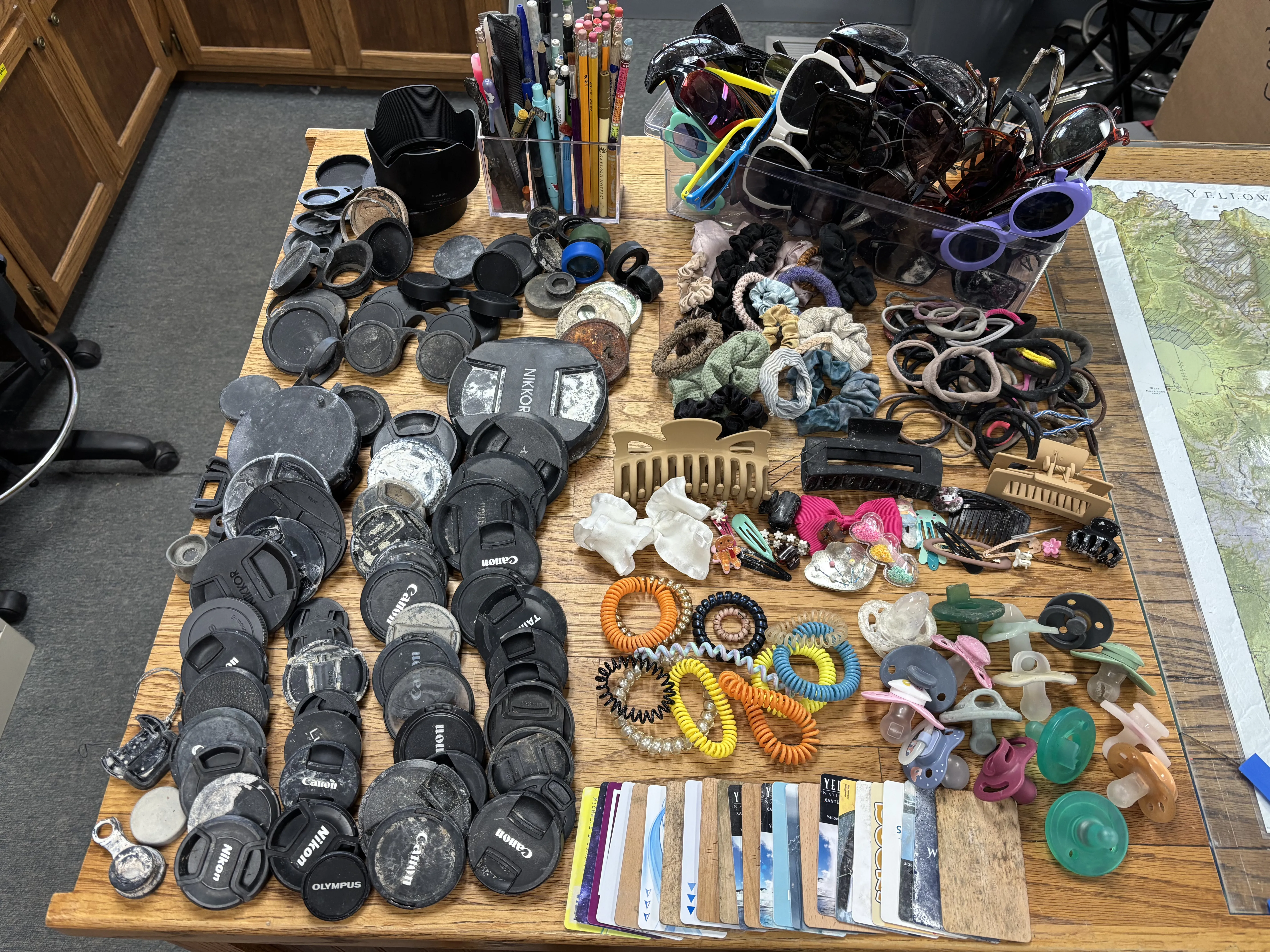 Frequent finds collected by the Yellowstone National Park Geology Team from hydrothermal areas during the summer season in 2026: camera lens covers and binocular parts, pens and pencils, sunglasses, hair accessories, hotel keys, and more! National Park Service photo by Margery Price, September 2026.