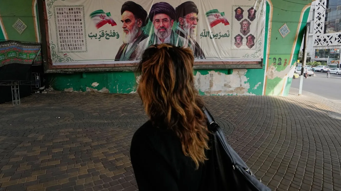 A woman walks past a banner showing portraits of the late Iranian revolutionary founder Ayatollah Khomeini, left, Supreme Leader Ayatollah Mojtaba Khamenei, center, and the late Supreme Leader Ayatollah Ali Khamenei in northern Tehran, Iran, Saturday, Sept. 12, 2026. (AP Photo/Vahid Salemi)