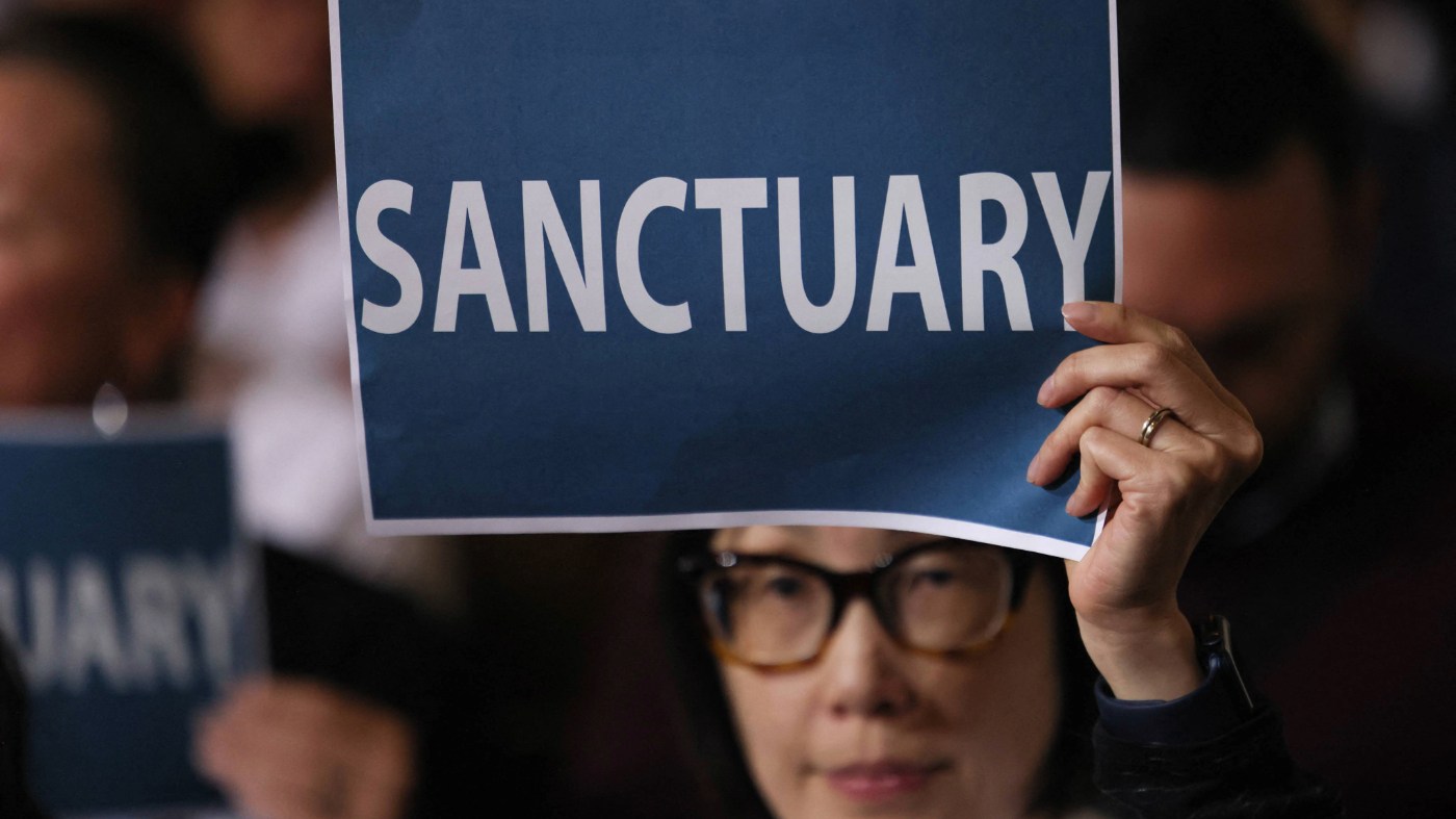 People in the audience hold up signs as the Los Angeles City Council considers a “sanctuary city” ordinance at City Hall in Los Angeles, California, on November 19, 2024. (Photo by Etienne LAURENT / AFP) (Photo by ETIENNE LAURENT/AFP via Getty Images)