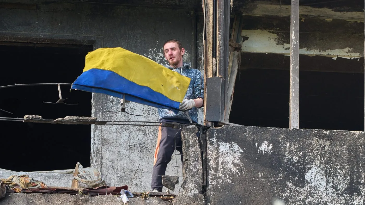 A man hangs out the national flag at his damaged apartment balcony after a missile strike during Russia’s night air attack in Kyiv, Ukraine, Oct. 14, 2026.