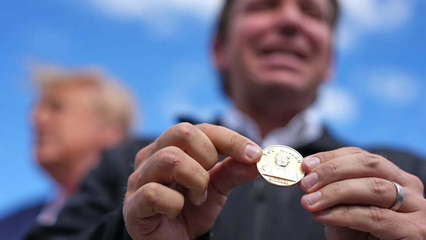 Florida Gov. Ron DeSantis holds a coin he presented to President Trump as they speak to reporters, Oct. 23, 2026, at Southwest Florida International Airport in Fort Myers, Fla.