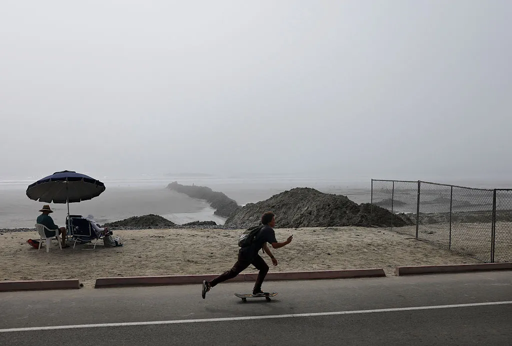 People sit (L) on what remains of an eroded beach as work continues on a sand replenishment project along the Pacific Ocean shoreline on October 7, 2026, in Oceanside, California. An emerging El Niño and active Pacific hurricane season are bringing significant coastal erosion and sand loss to Southern California beaches, with experts warning the situation could worsen this winter. In addition, an oceanic Kelvin wave is moving up the coastline, while remnants of Hurricane Rachel are projected to impact the region this weekend. (Photo by Mario Tama/Getty Images)