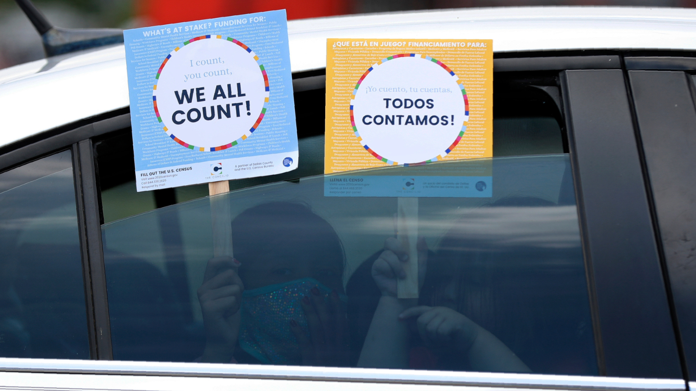 Two young children hold signs through the car window that make reference to the 2020 U.S. census as they wait in the car with their family at an outreach event in Dallas, June 25, 2020.
