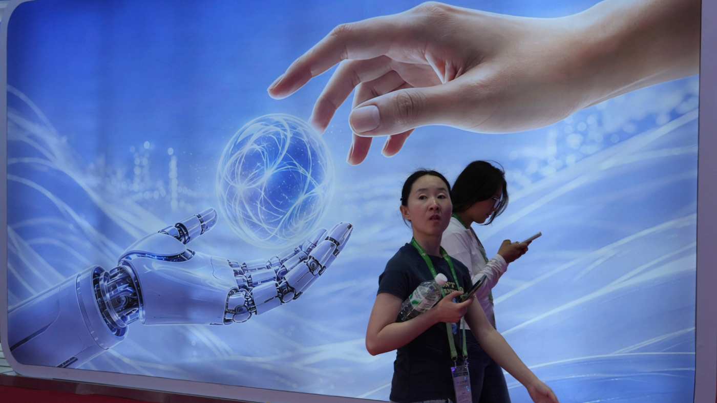 Visitors walk past a display depicting artificial intelligence and a human hand at the China International Supply Chain Expo in Beijing on Monday, June 22, 2026. (AP Photo/Ng Han Guan)