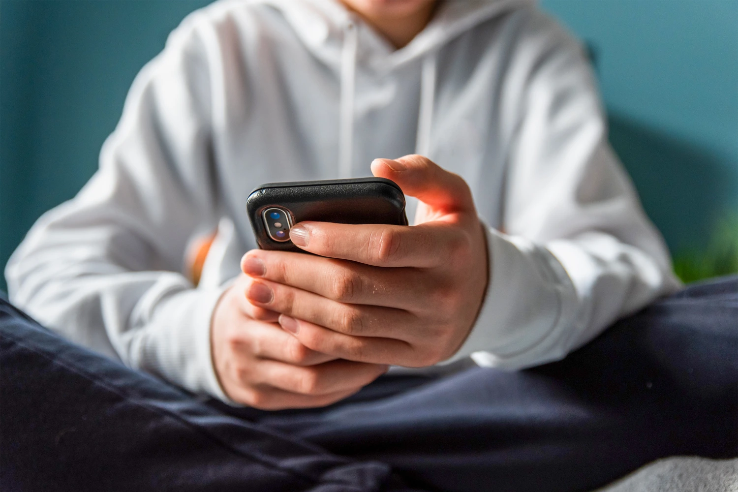Close up of hands of teen boy in white sweater texting on phone.