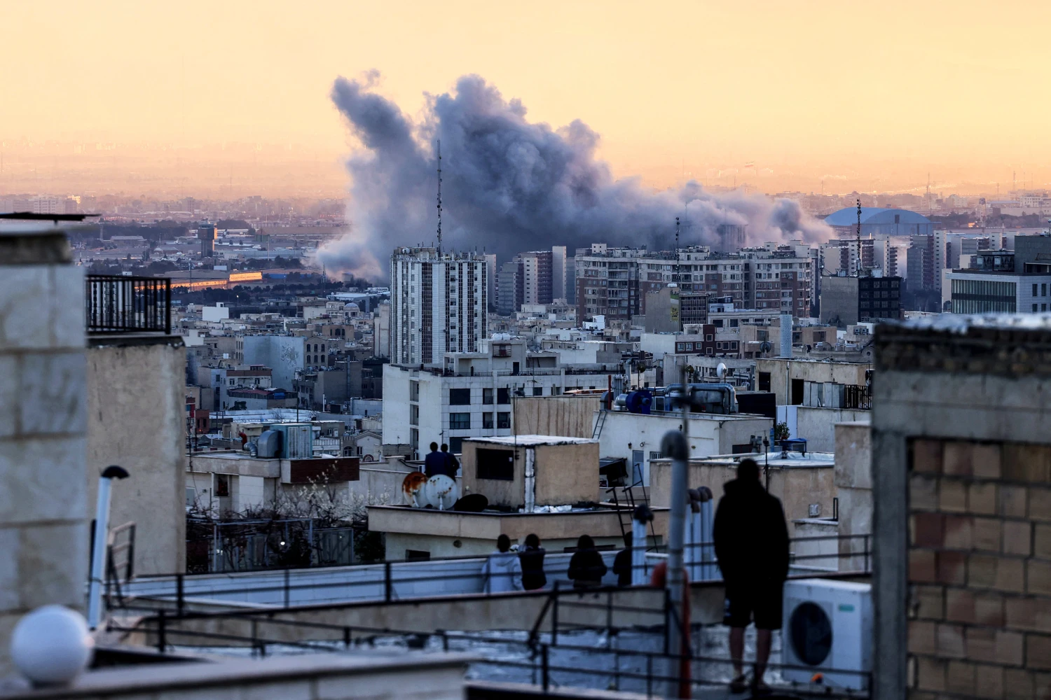 A person stands on the roof of a building looking at a plume of smoke rises after a strike on the Iranian capital Tehran, on March 3, 2026.