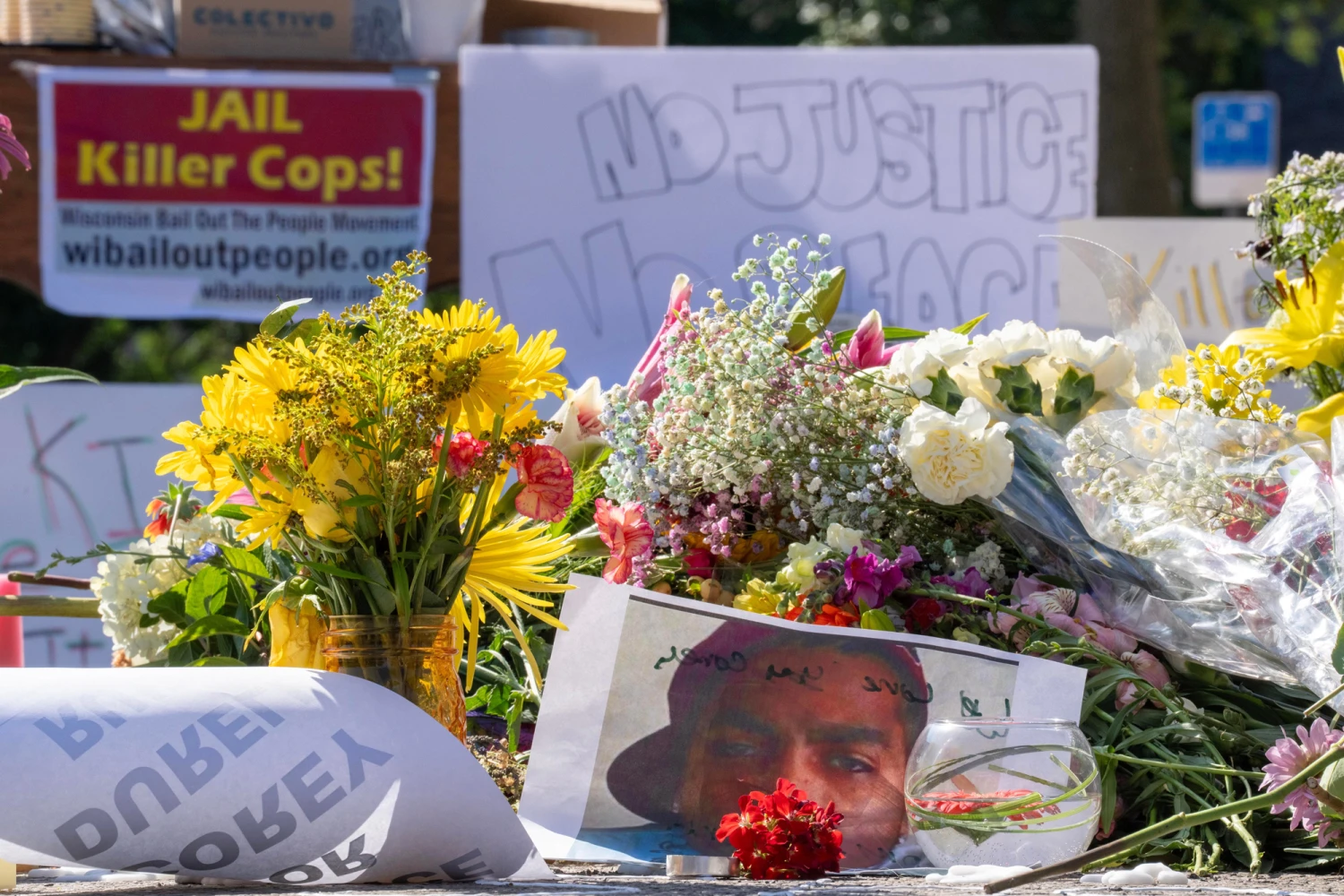 The day after police shot and killed a man armed with a knife, people gather around a memorial on July 23, 2026, at the intersection of Williamson and South Baldwin Streets in Madison, Wis.