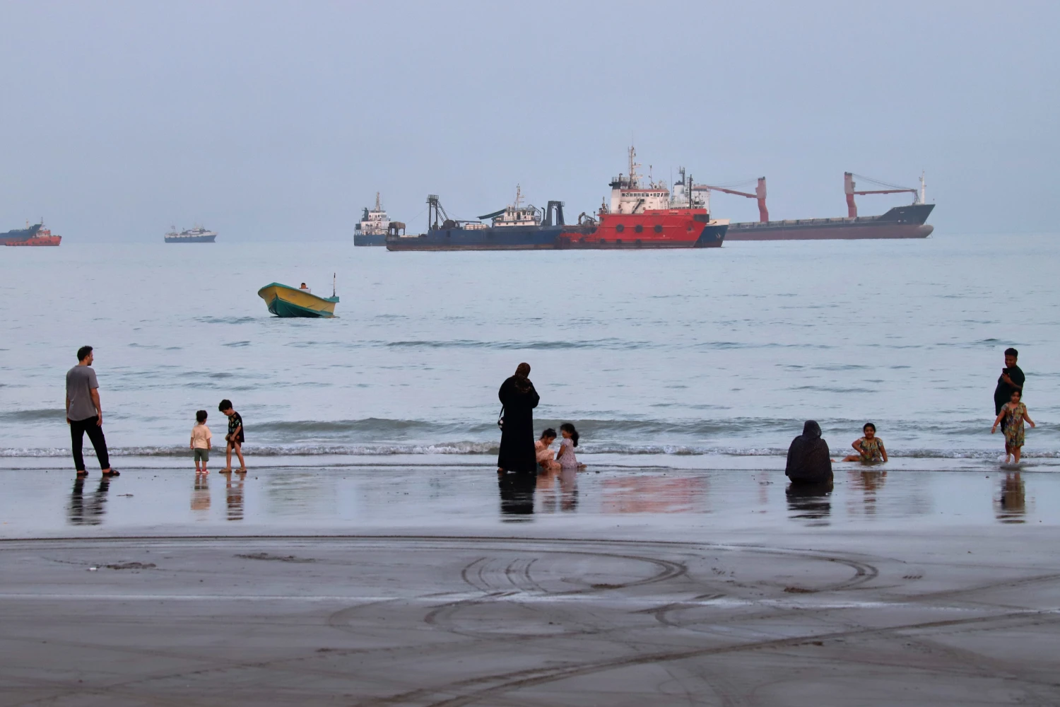 People spend time at a beach as commercial vessels are anchored in the Strait of Hormuz off Bandar Abbas, Iran, Wednesday, Aug. 5, 2026.