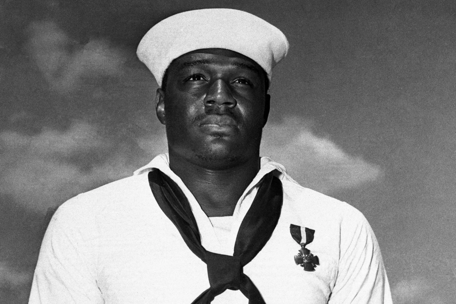 The unnamed hero of Pearl Harbor, a messman with the United States Fleet, has been identified as Dorie Miller of Waco, Texas, seen here wearing the cross he received at a ceremony.  When Japanese planes bombed his ship in Pearl Harbor, Miller manned a machine gun, although he had received no training in the use of the weapon.  He stuck to his post until his dying Captain ordered all hands to quit the stricken vessel.