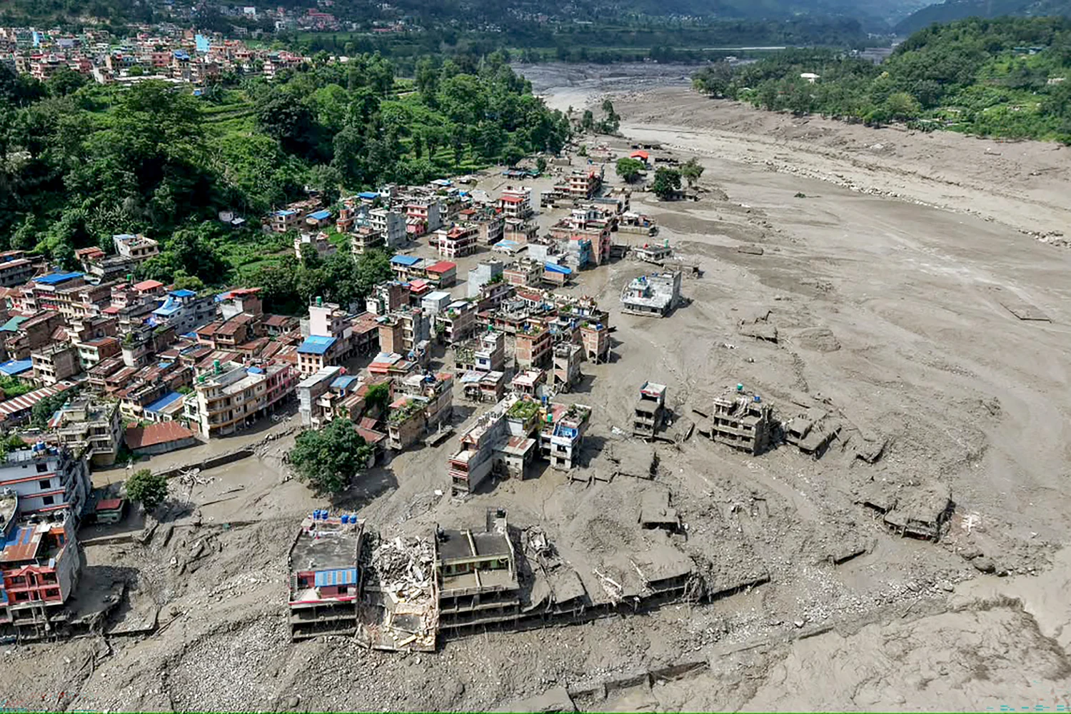TOPSHOT - Houses lie partially submerged in muddy water along a riverside after flash floods at Trishuli Bazar in Nepal's Nuwakot district on August 26, 2026.
