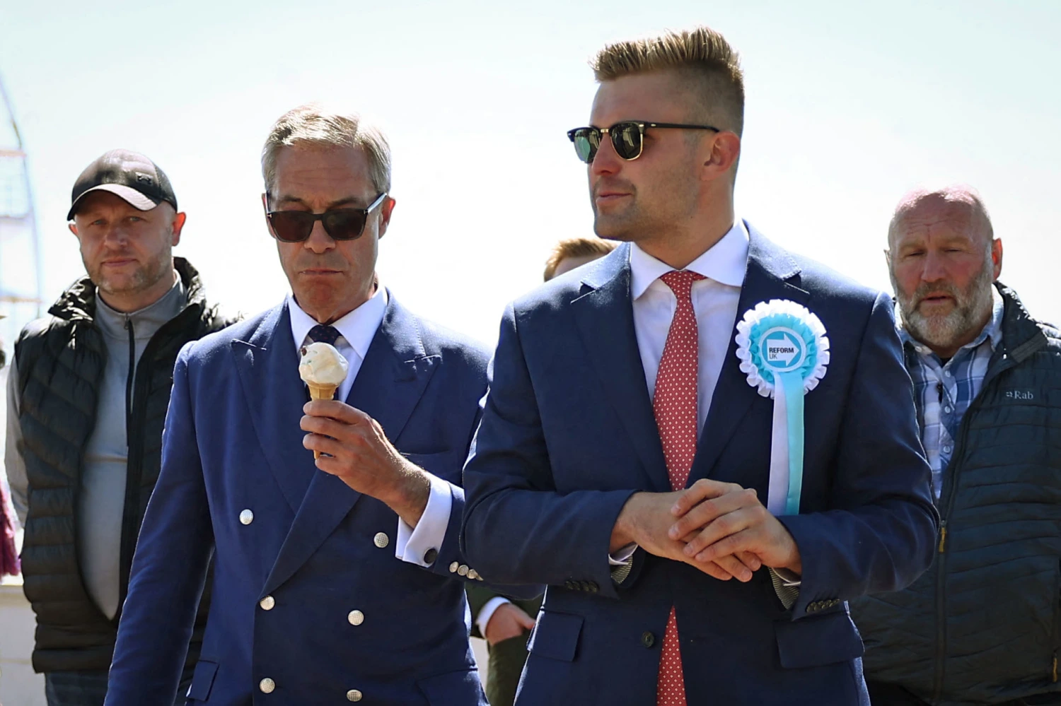 Reform UK leader Nigel Farage eats an ice cream cone as he walks walks with Dan Jukes, second from right, in Clacton-on-Sea, England, on July 4, 2024.