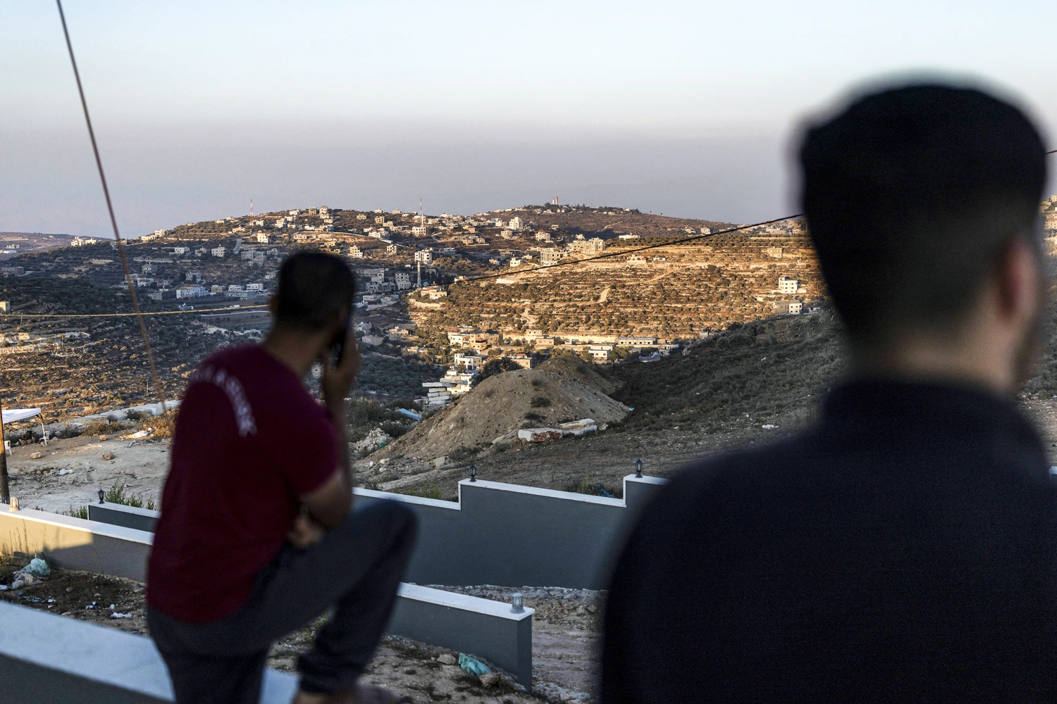 Palestinian men watch Israeli army soldiers from the roof of one of the Palestinian homes besieged by Israeli settlers in the occupied West Bank village of Qusra on August 18, 2026.