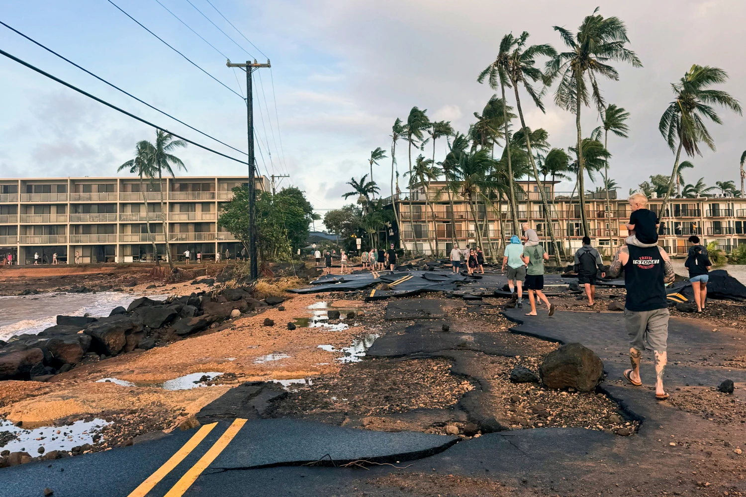 People walk past damage caused by Hurricane Lowell on Tuesday, Sept. 8, 2026 in Poʻipū on Kauaʻi's south shore, in Hawaii.