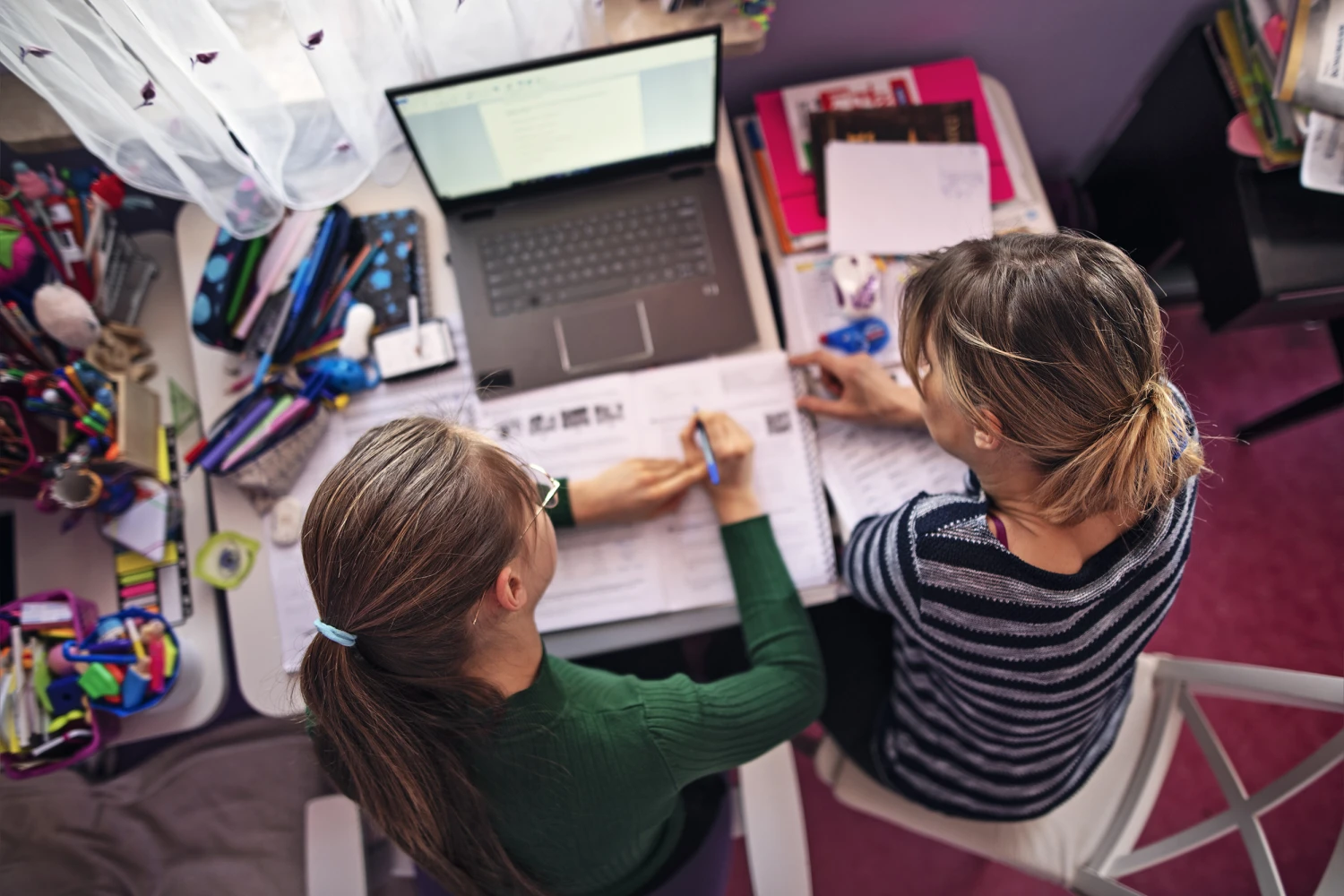 Teenage girl doing homework in her room with help of her mother.
