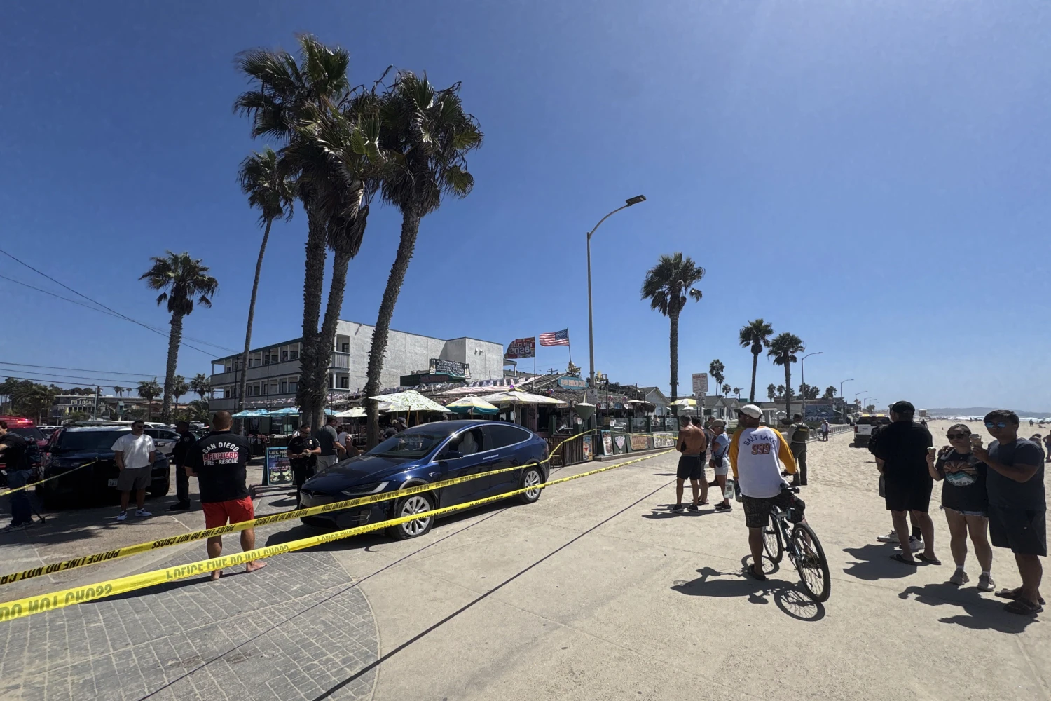 Bystanders look onto the scene in Pacific Beach after a blue Tesla drove up onto the boardwalk near Baja Beach Cafe on Thomas Ave., Sept. 14, 2026.