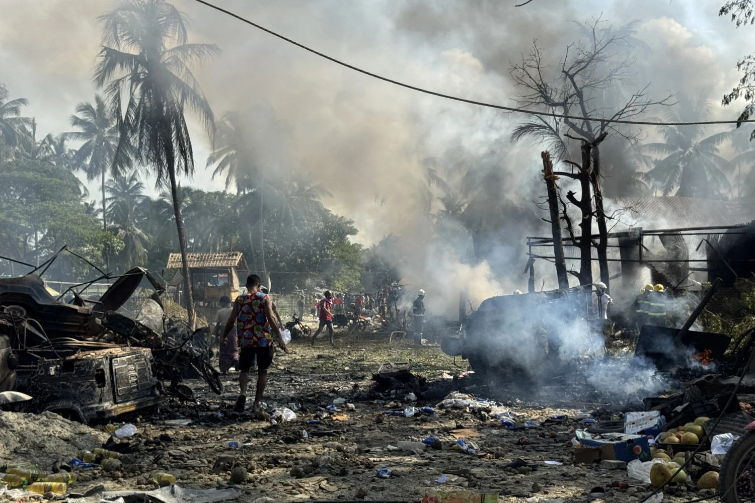 People walk through smoke and smouldering debris following a military airstrike on a market and adjacent bridge in Kyauktaw, Western Rakhine state on Sept., 28, 2026.