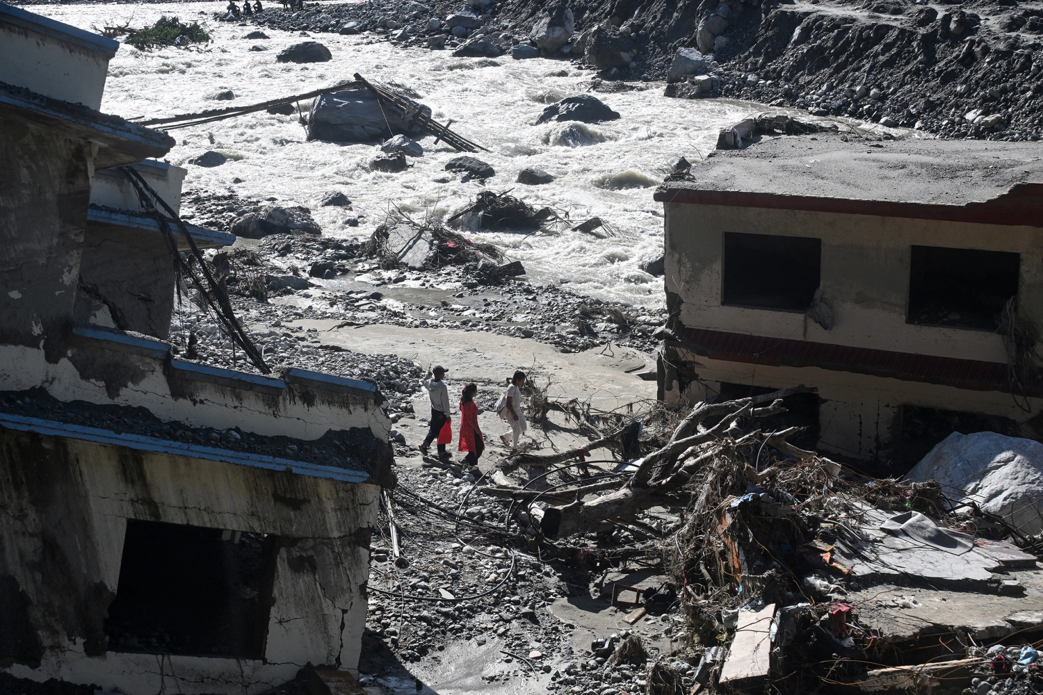 People walk past damaged houses covered in sludge in the aftermath of the August 26 flash flood, at Betrawati Bazaar in Nepal's Rasuwa district on September 28, 2026.