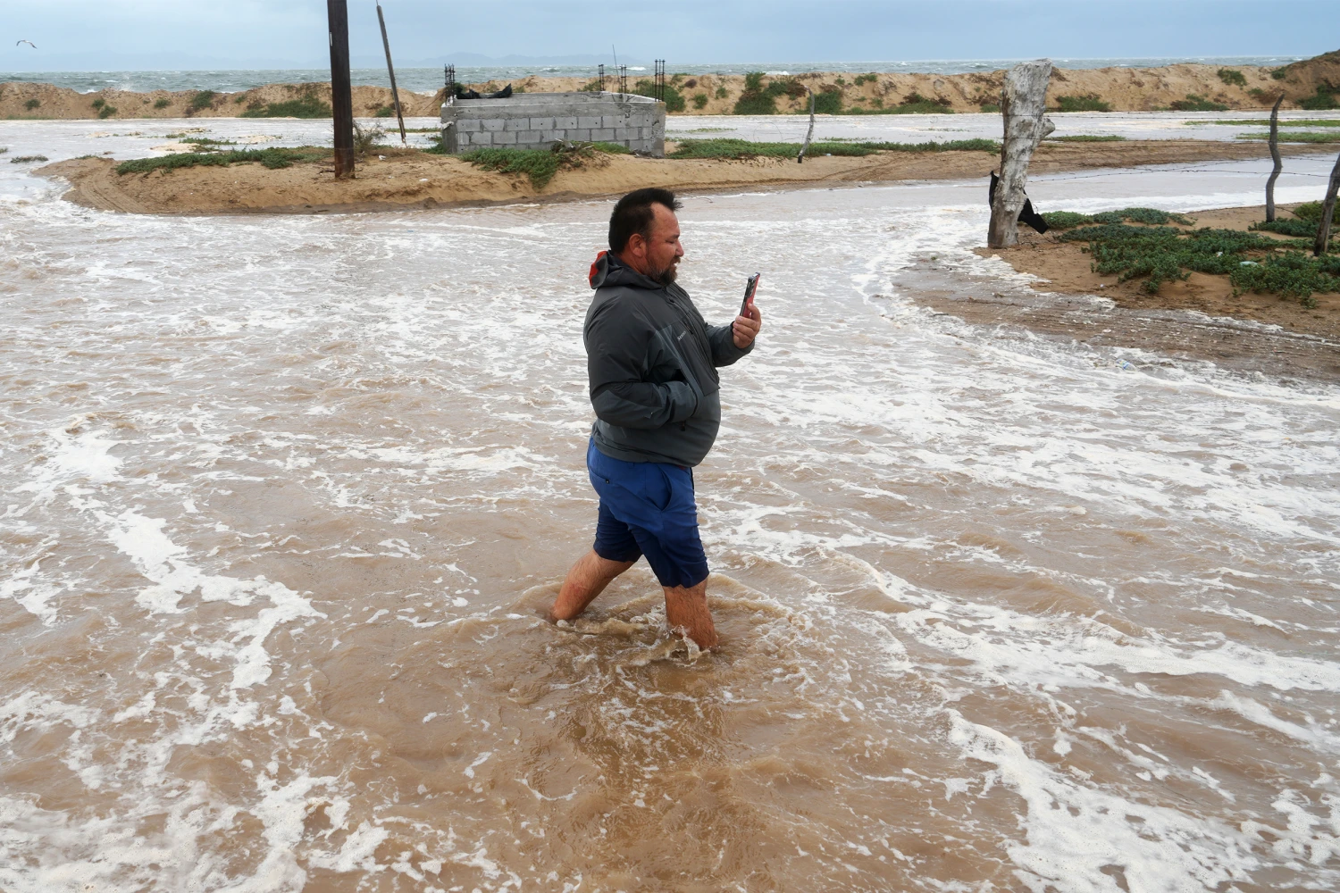 A man walks on a street next to the beach as he wades through water brought by Hurricane Polo in Puerto San Carlos, Baja California Sur state, Mexico, Monday, Sept. 28, 2026.