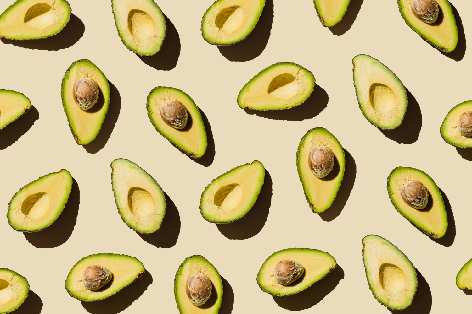 Pattern of fresh ripe green avocado fruit halves on beige background. Healthy food, diet and detox concept. Flat lay, top view