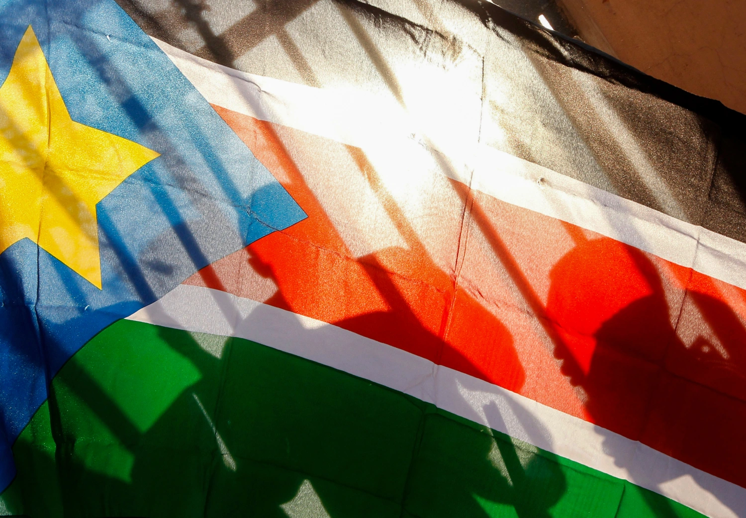 The silhouettes of South Sudanese people are seen through a South Sudanese flag as they line up to cast their votes in Juba, South Sudan, Jan. 9, 2011.