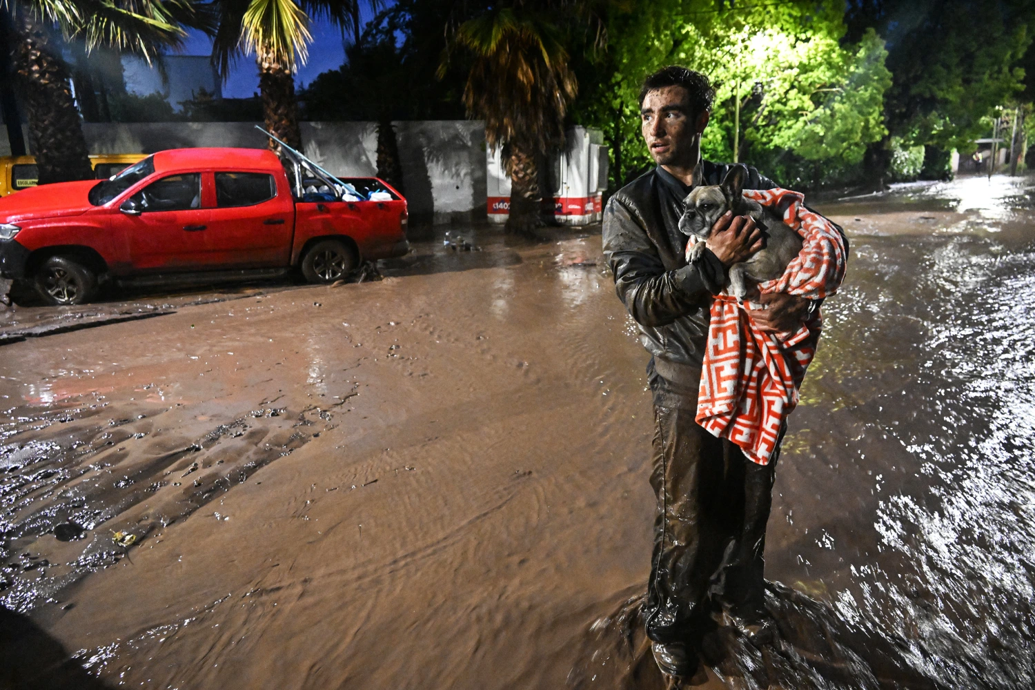 A man carrying an dog through a flooded street following a mudslide in the Las Condes district of Santiago on October 8, 2026.