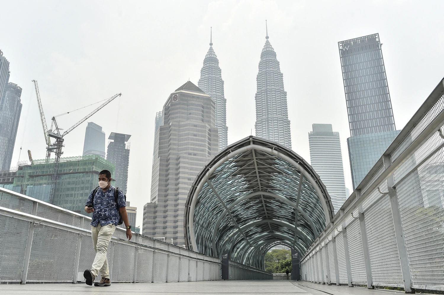A man walks along a pedestrian bridge with the Petronas Twin Tower partially obscured by haze in the background in Kuala Lumpur on October 7, 2026.