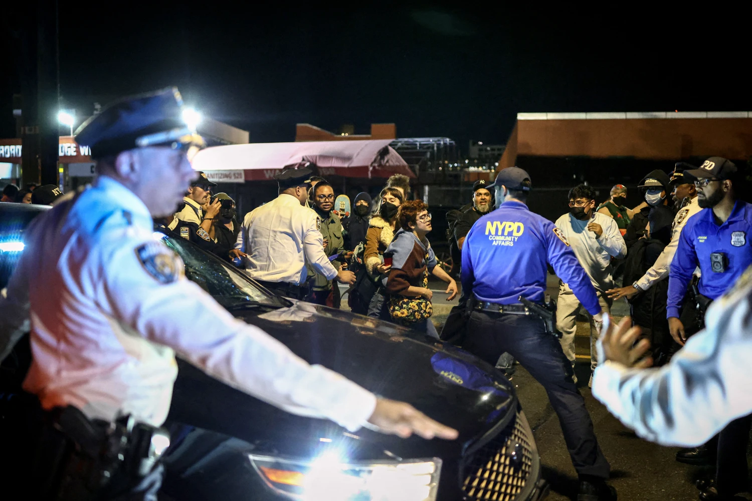 NYPD officers attempt to stop protesters from blocking a car containing federal law enforcement officers as it leaves the scene where a man was shot by an ICE officer in New York Cityon Oct. 8, 2026.