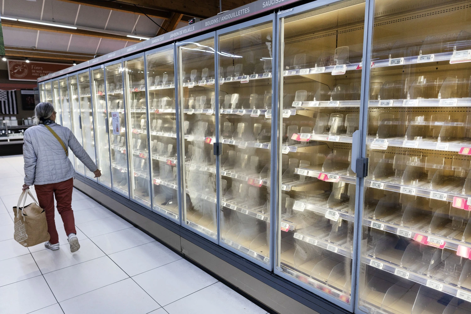 A woman walks past empty fresh-food refrigerators at an Intermarché supermarket in Névez, western France, on October 12, 2026, following a cyberattack affecting the French supermarket chains Intermarché and Cooperative U that caused their refrigerators to defrost.