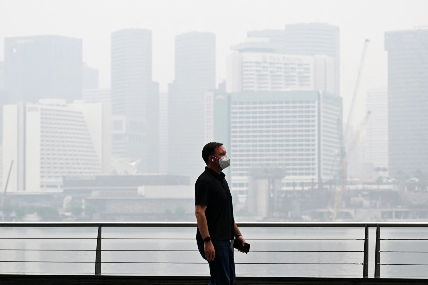 A pedestrian wearing a mask walks along the boulevard at Marina bay as buildings are seen shrouded with haze in Singapore on October 12, 2026.