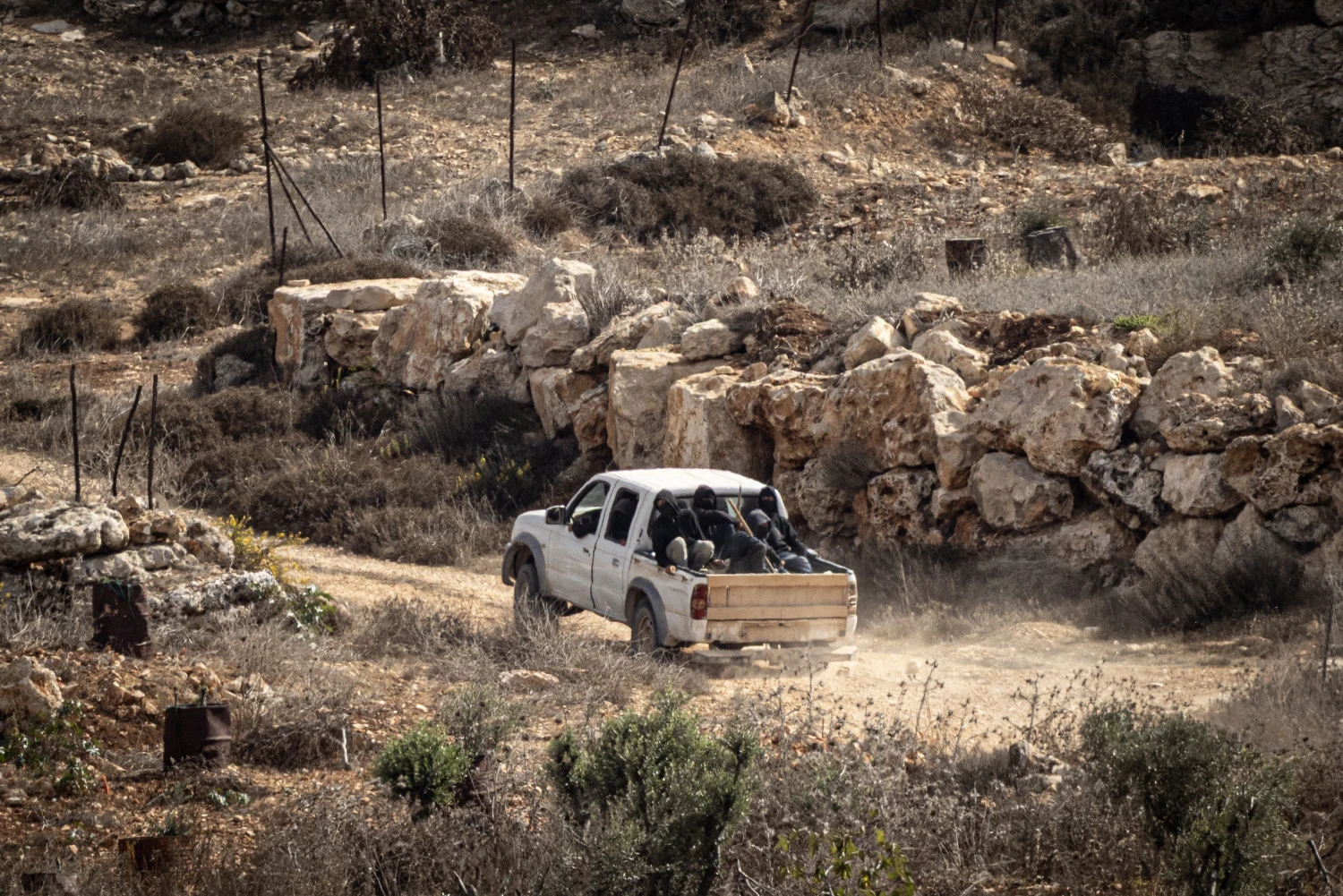 Masked Israeli settlers armed with clubs drive around in an unlicensed pickup car during the olive harvest on Oct. 17 in Abu Falah, West Bank.