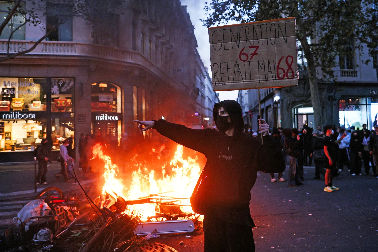 A protester holds a sign reading "Generation 6-7 redoes May 68" in front of a fire at the Boulevard des Capucines in Paris on Saturday.