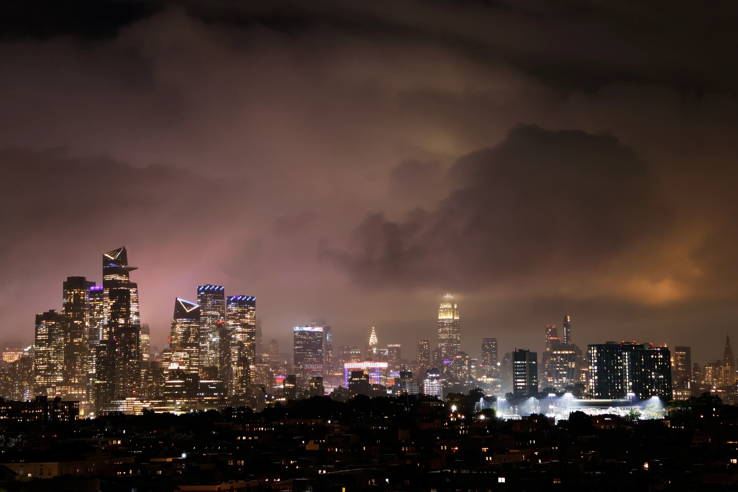 Storm clouds illuminated by the lights of midtown Manhattan pass over Hudson Yards and the Empire State Building in New York City on October 16, 2026, as seen from Jersey City, New Jersey.