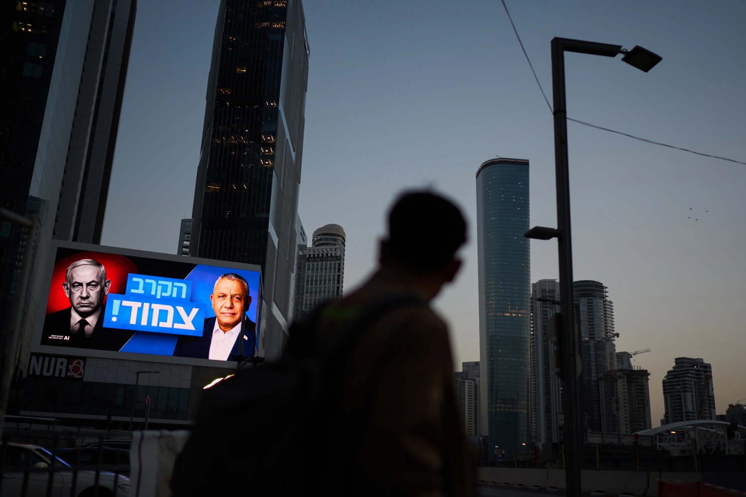 A pedestrian passes a campaign billboard featuring Israeli Prime Minister Benjamin Netanyahu, left, and his main rival, opposition candidate Gadi Eisenkot, with a message in Hebrew that reads "The race is tight," Friday, Oct. 23, 2026, in Tel Aviv, Israel.