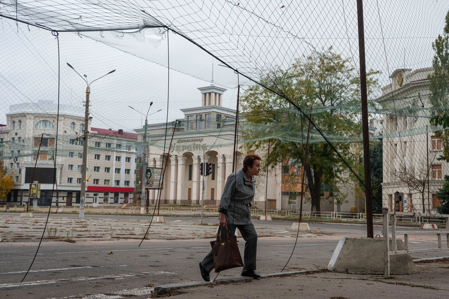 A woman walks on a sidewalk beneath anti-drone nets stretched over a street during a local ceasefire related to evacuation efforts in Oleshky, in Kherson, Ukraine, Tuesday, Oct. 27, 2026.