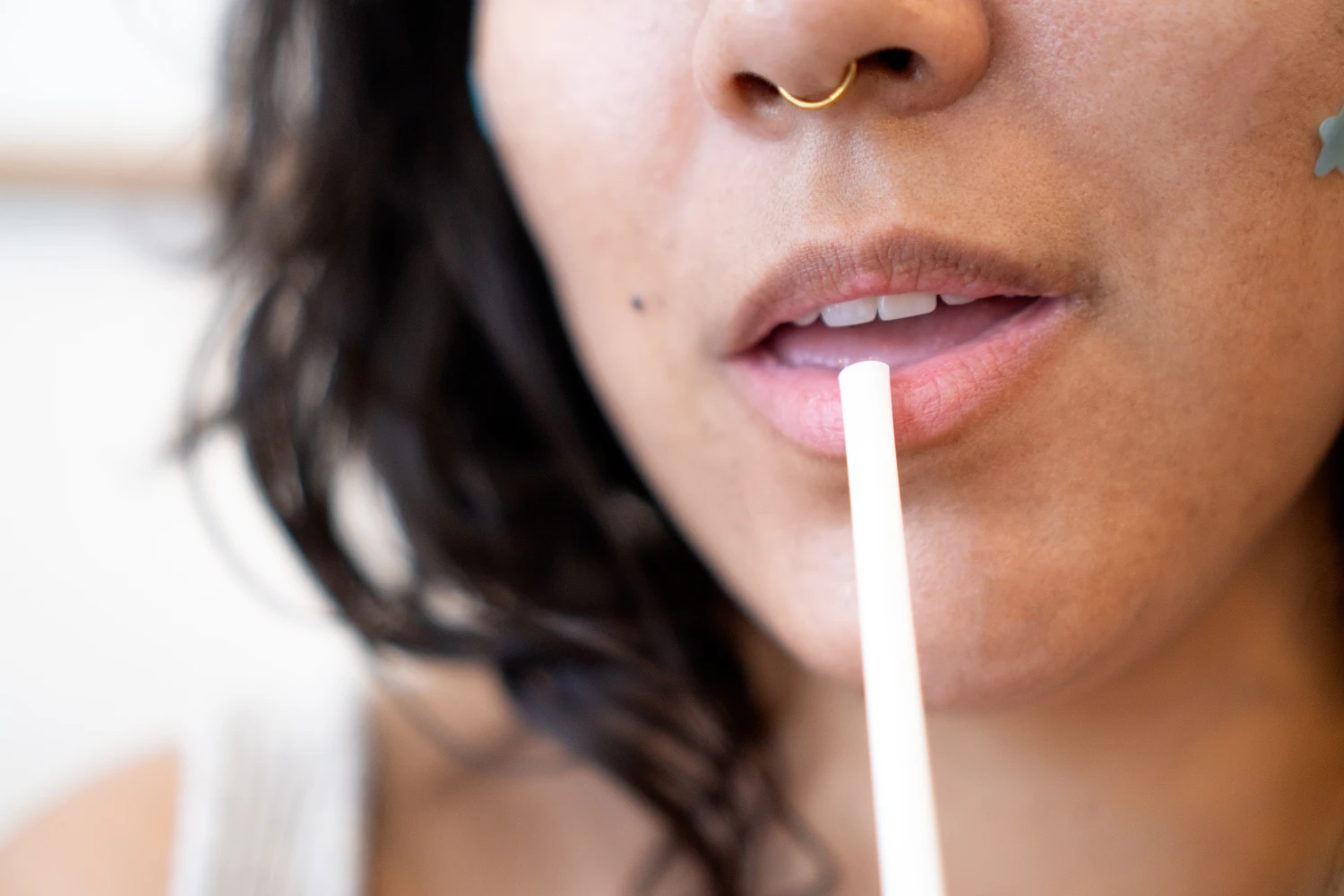 Young woman with natural curly hair and a septum piercing drinking from a straw. Wellness and breakfast concept