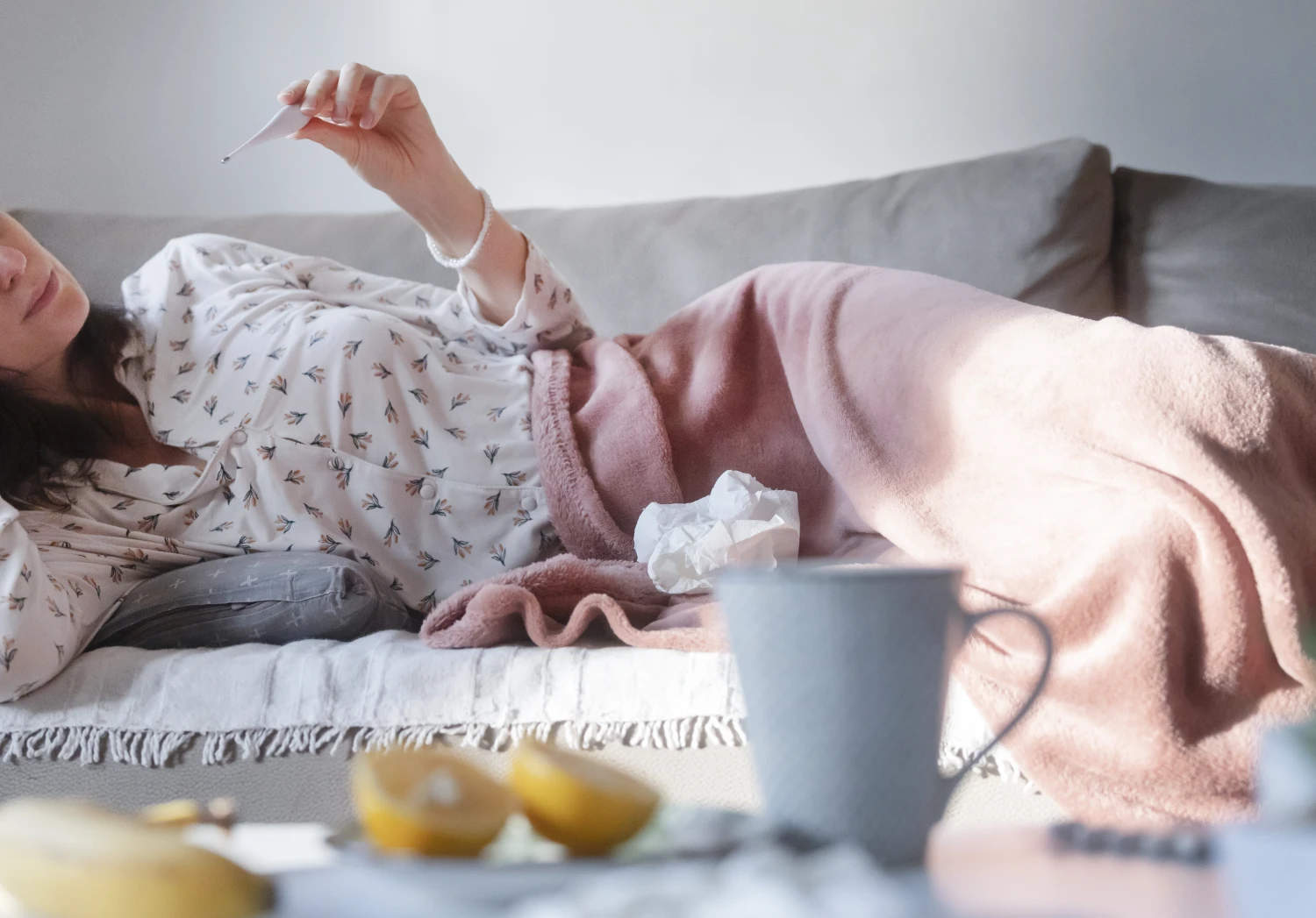 Young woman checking her temperature while lying on the couch at home
