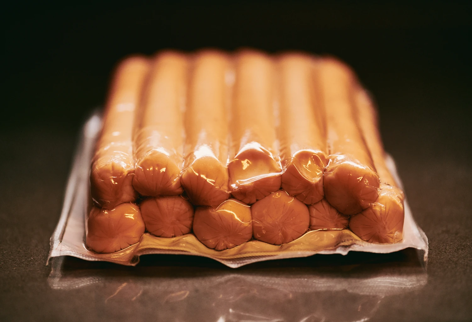 A tightly vacuum-sealed package of sausages neatly arranged in rows, preserving freshness and texture. Ideal for meal preparation or storage in a modern kitchen setting.