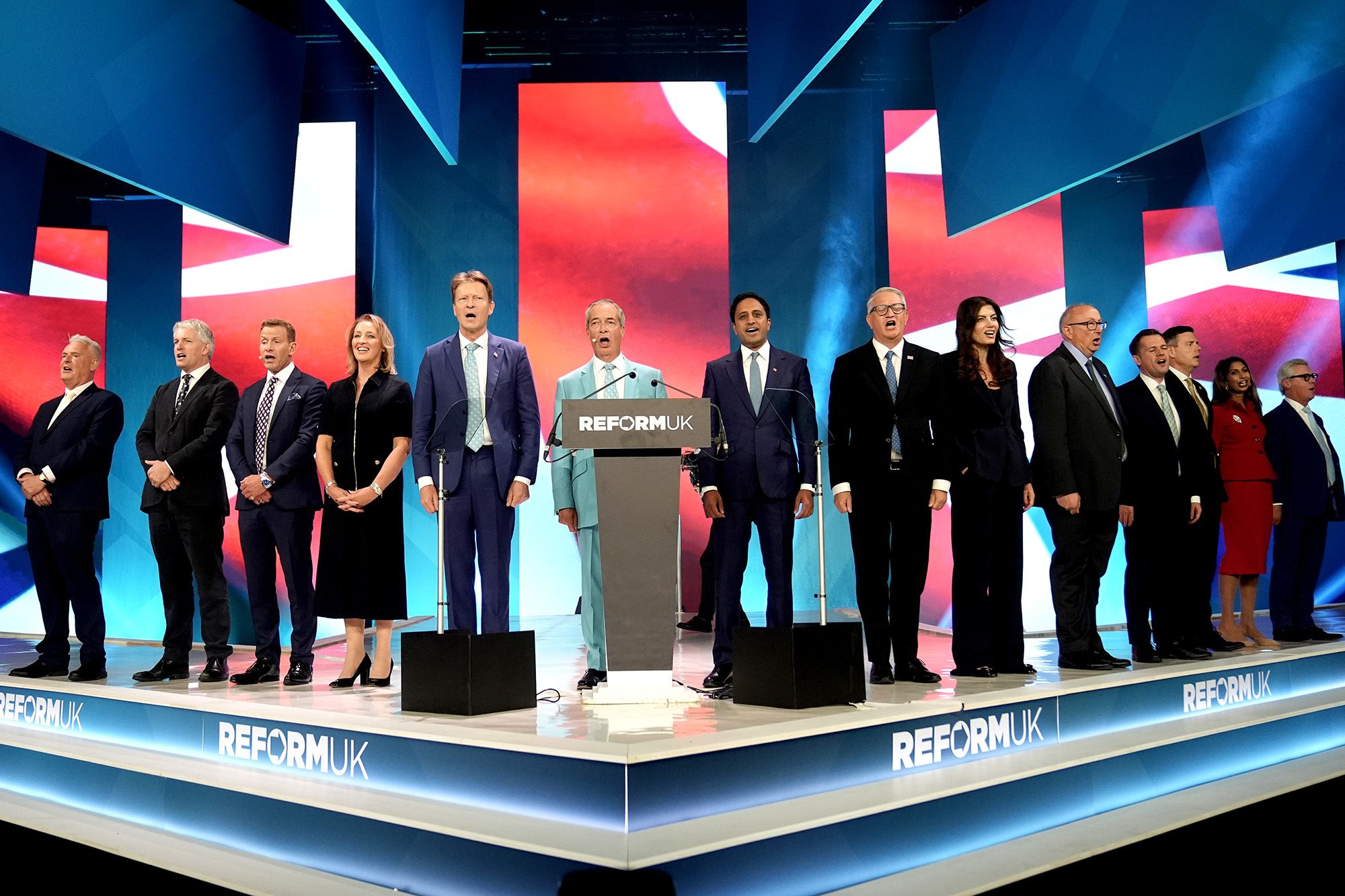 Reform UK leader Nigel Farage (centre) sings the national anthem with Reform UK chairman Lee Anderson (left), Sarah Pochin, MP for Runcorn and Helsby (fourth from left), Reform UK deputy leader Richard Tice (fifth from left), Reform UK home affairs spokesman Zia Yusuf (seventh from left), Reform UK London mayoral candidate Laila Cunningham (ninth from left), Reform UK Treasury spokesman Robert Jenrick (eleventh from left), Reform UK education spokesperson Suella Braverman (second from right), Leader of Reform UK Scotland Malcolm Offord (right) and Reform UK party members during the Reform UK National Conference, at the National Exhibition Centre in Birmingham. Picture date: Saturday September 5, 2026. PA Photo. Photo credit should read: Stefan Rousseau/PA Wire POLITICS (Press Association via AP Images)