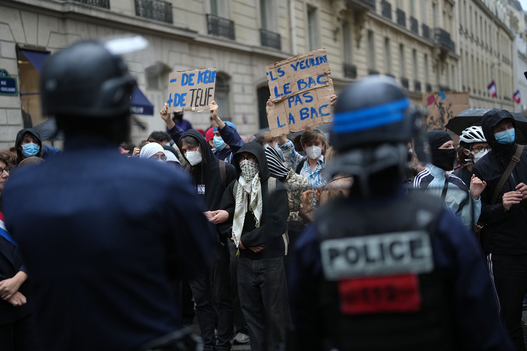 Police stand guard as a student holds a board reading 'they want the BAC (High School Diploma) Not the BAC (Anti-criminality units)' during a protest against under-resourced schools, in Paris, on Wednesday.