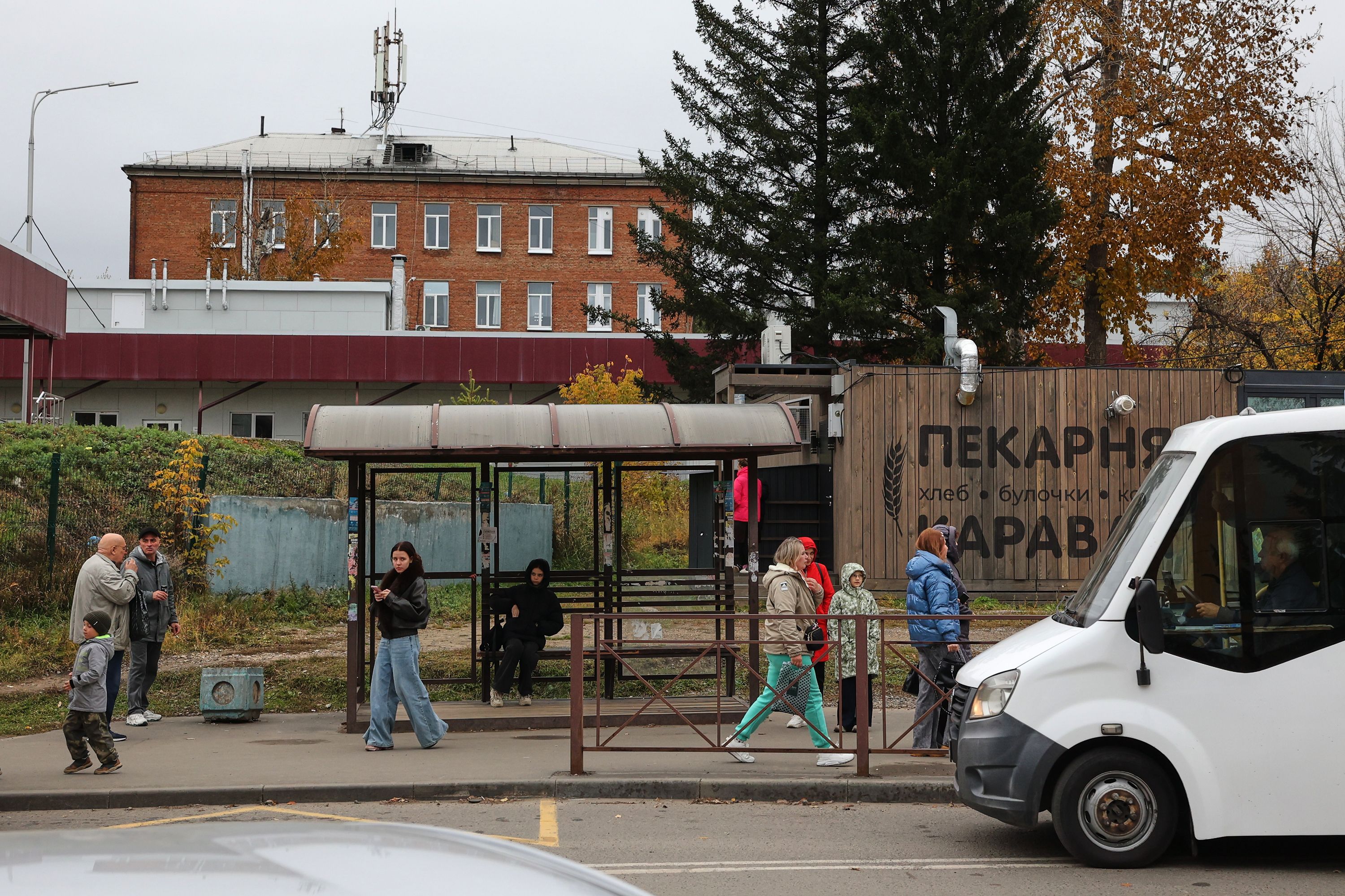 People are seen at a bus stop in Shelekhov, a Russian town near the city of Irkutsk, on Thursday, backdropped by the district hospital and the medical center for treating infectious diseases.