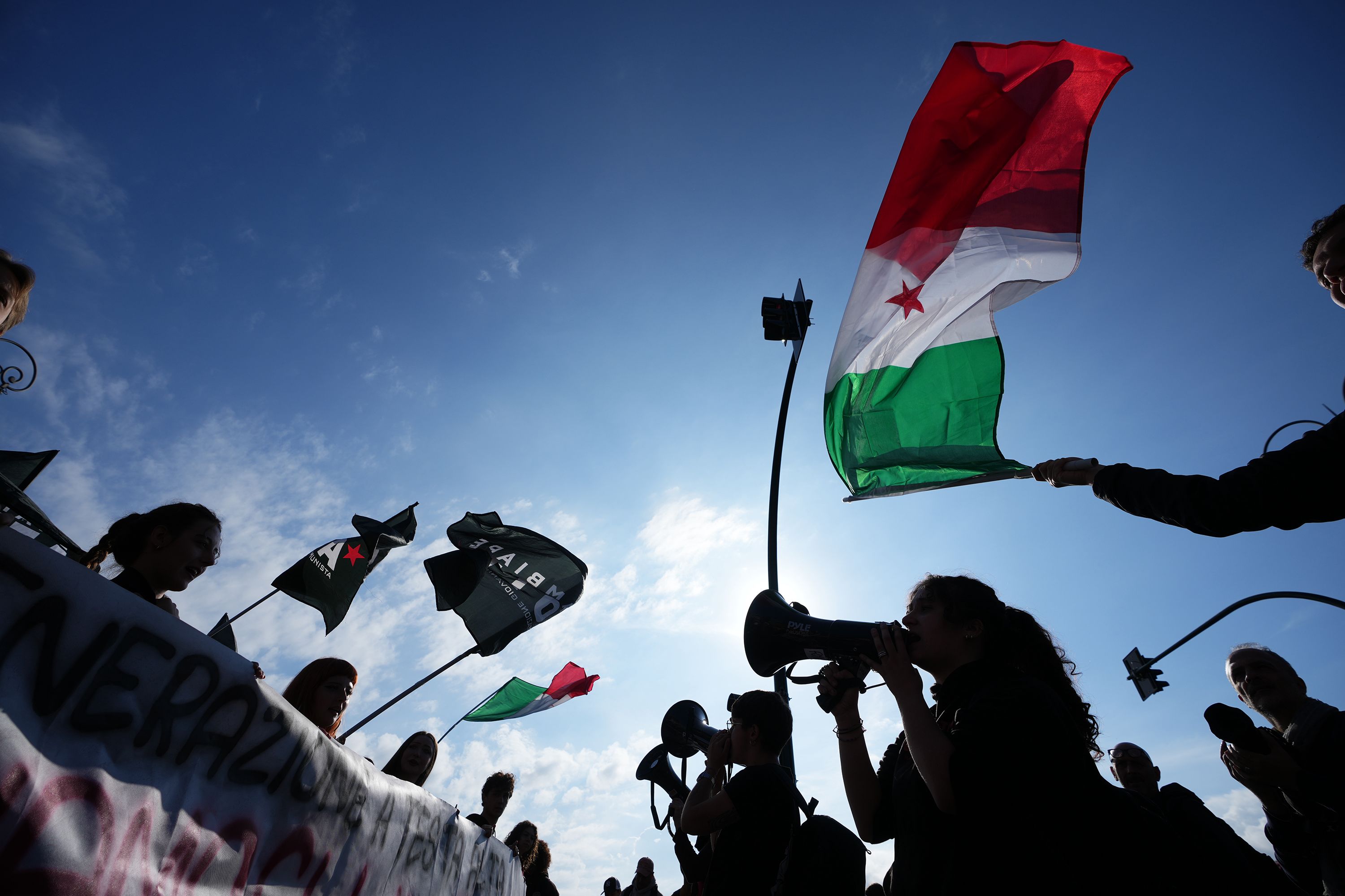 Demonstrators wave flags and shout slogans through megaphones during a nationwide general strike called by grassroots unions to protest rising living costs, low wages and military spending in Rome, Friday, Oct. 30.