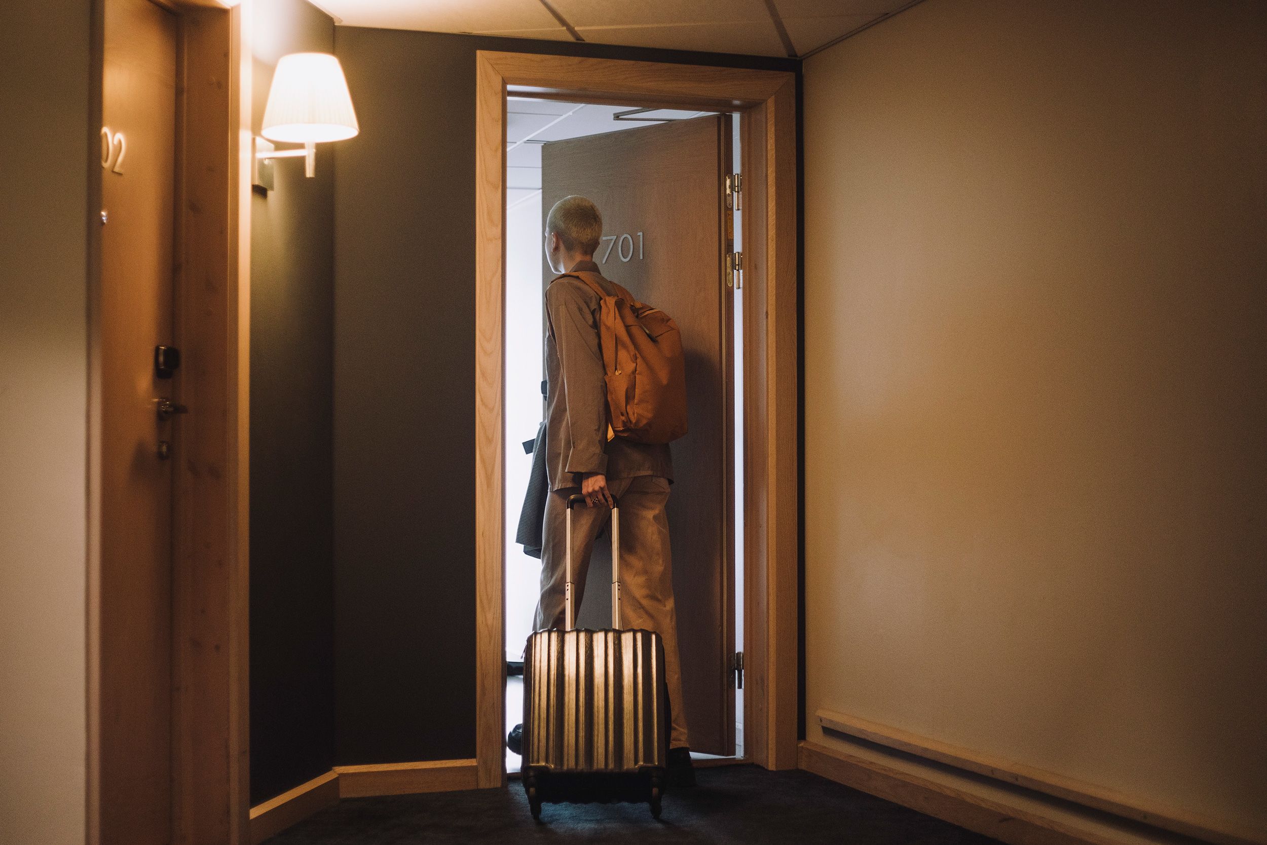 Non-binary business person with luggage entering hotel room